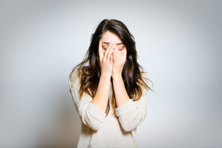 A woman with hands over her face, representing someone experiencing trauma.